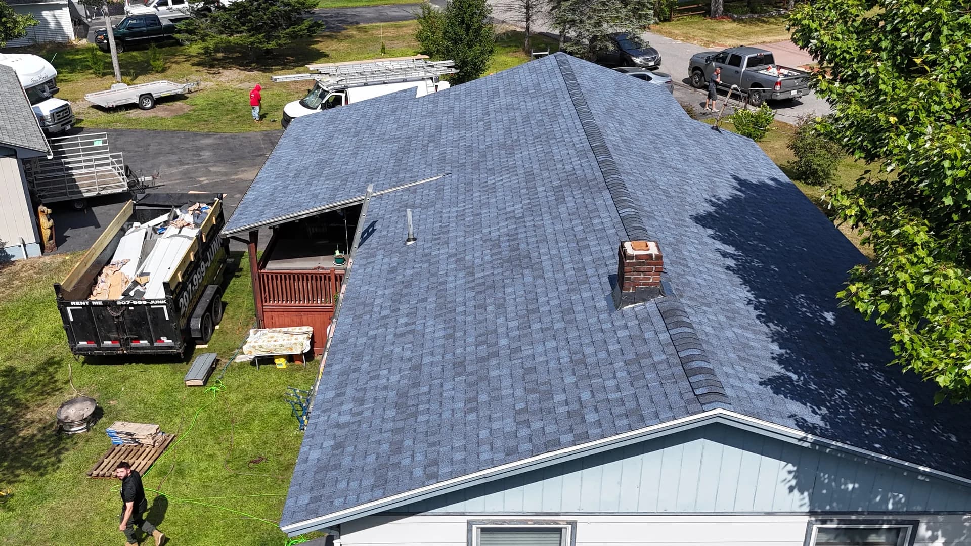Completed architectural shingle roof replacement in Maine - aerial drone view showing gray shingles with brick chimney