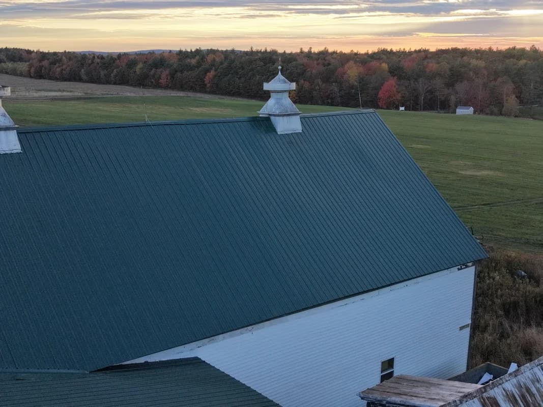 Green standing seam metal roof on Maine barn with cupolas at sunset - agricultural roofing